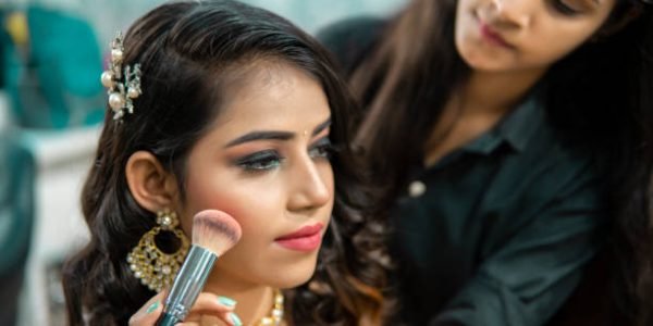 Female makeup artist doing makeup of a beautiful Indian woman for a wedding reception at the beauty parlor.